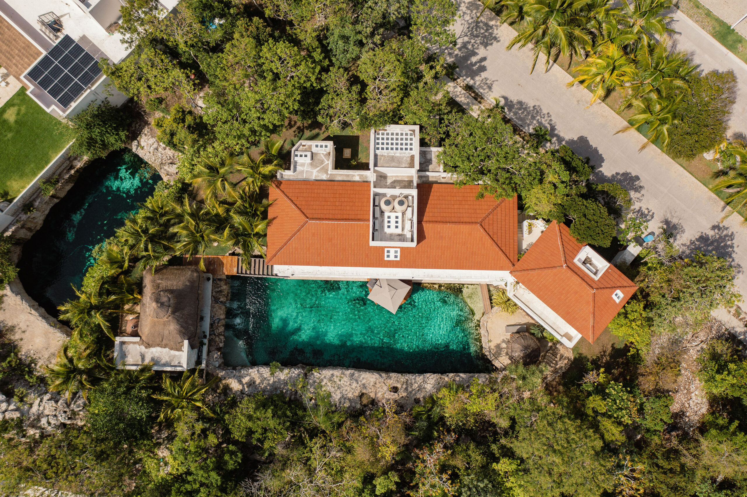 Aerial view of Casa Piedra de Agua, its terracotta-roofed villa set between a turquoise private cenote and the surrounding jungle in Puerto Aventuras