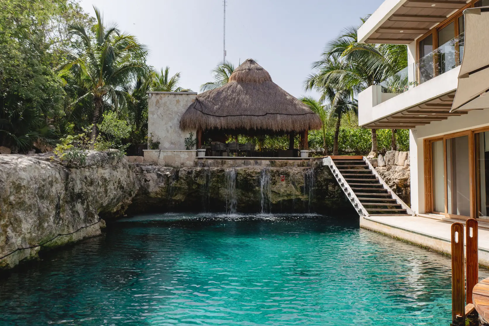 The private cenote at Casa Piedra de Agua, its turquoise water framed by natural limestone walls, a small waterfall and a palapa