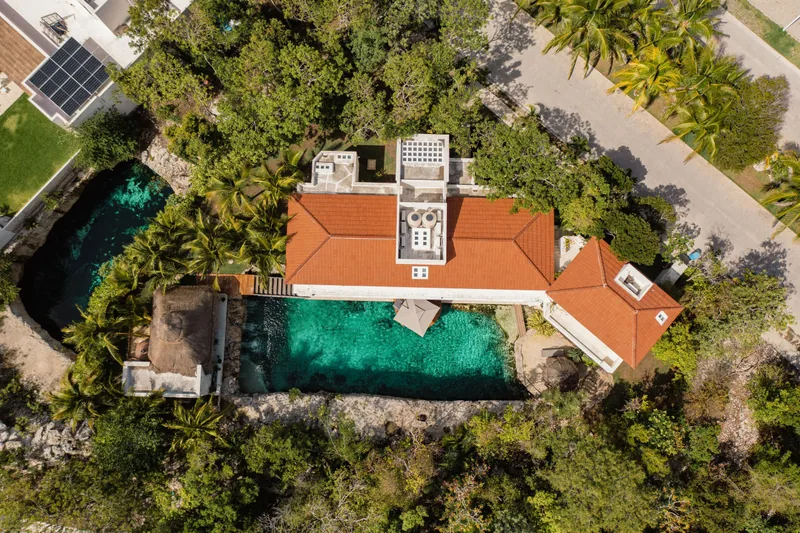 Aerial view of Casa Piedra de Agua, its terracotta-roofed villa set between a turquoise private cenote and the surrounding jungle in Puerto Aventuras